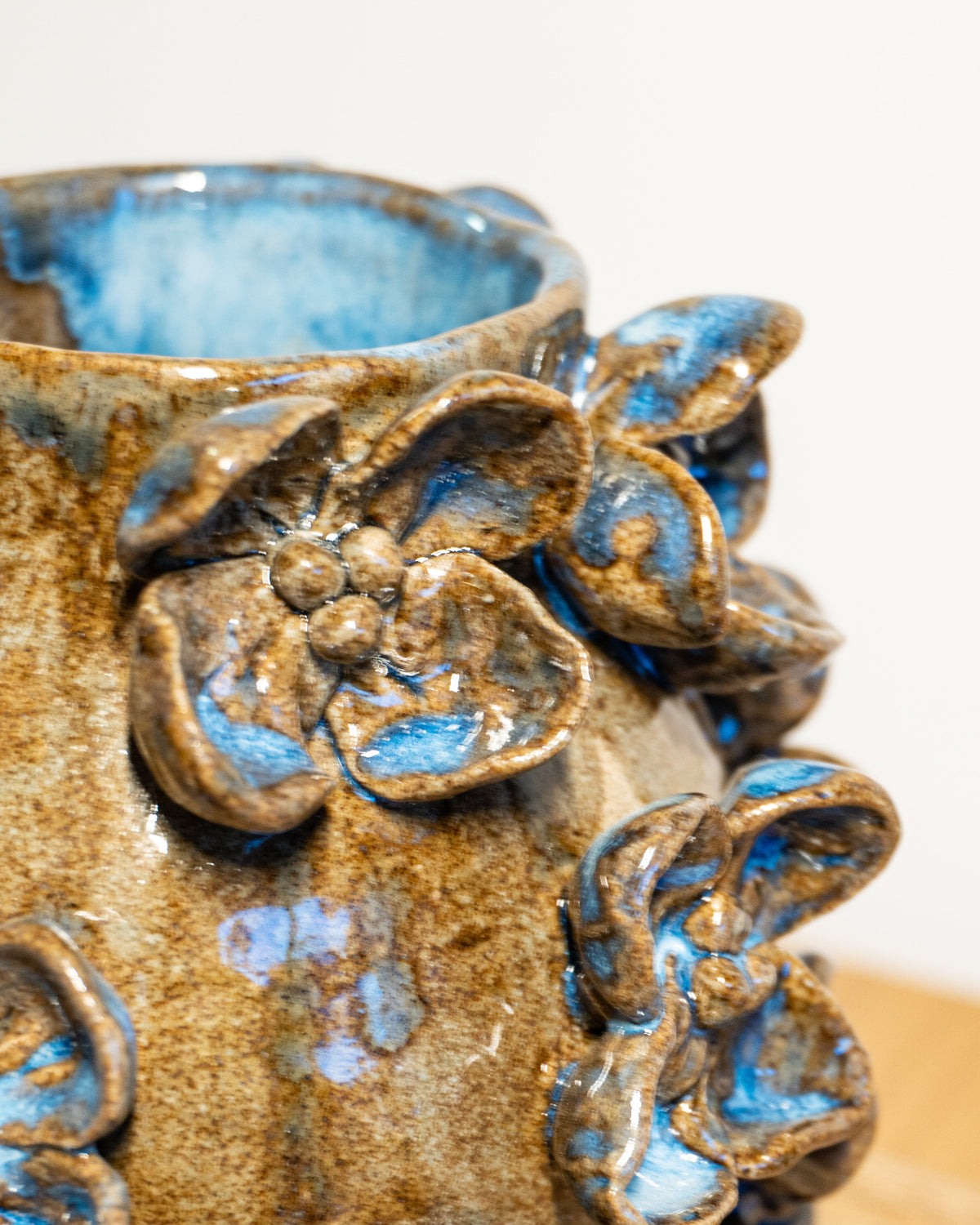 Close-up of a handmade ceramic pot with raised floral details, featuring a brown and blue glaze.