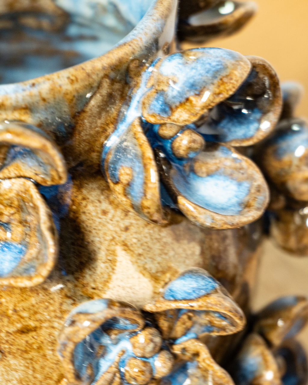 Close-up of a handmade ceramic vessel with raised floral details, featuring a glossy blue and tan glaze.