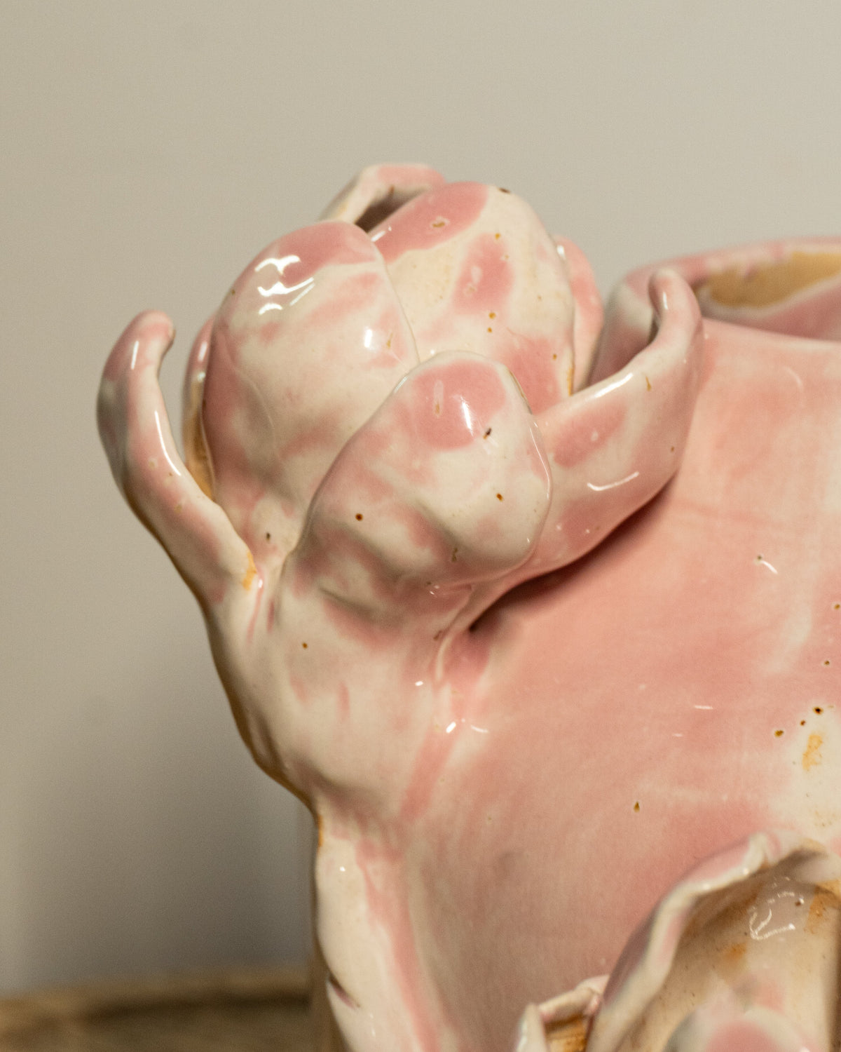 Close-up of a glossy pink and white ceramic vase with a sculpted flower, shown against a plain light gray background.
