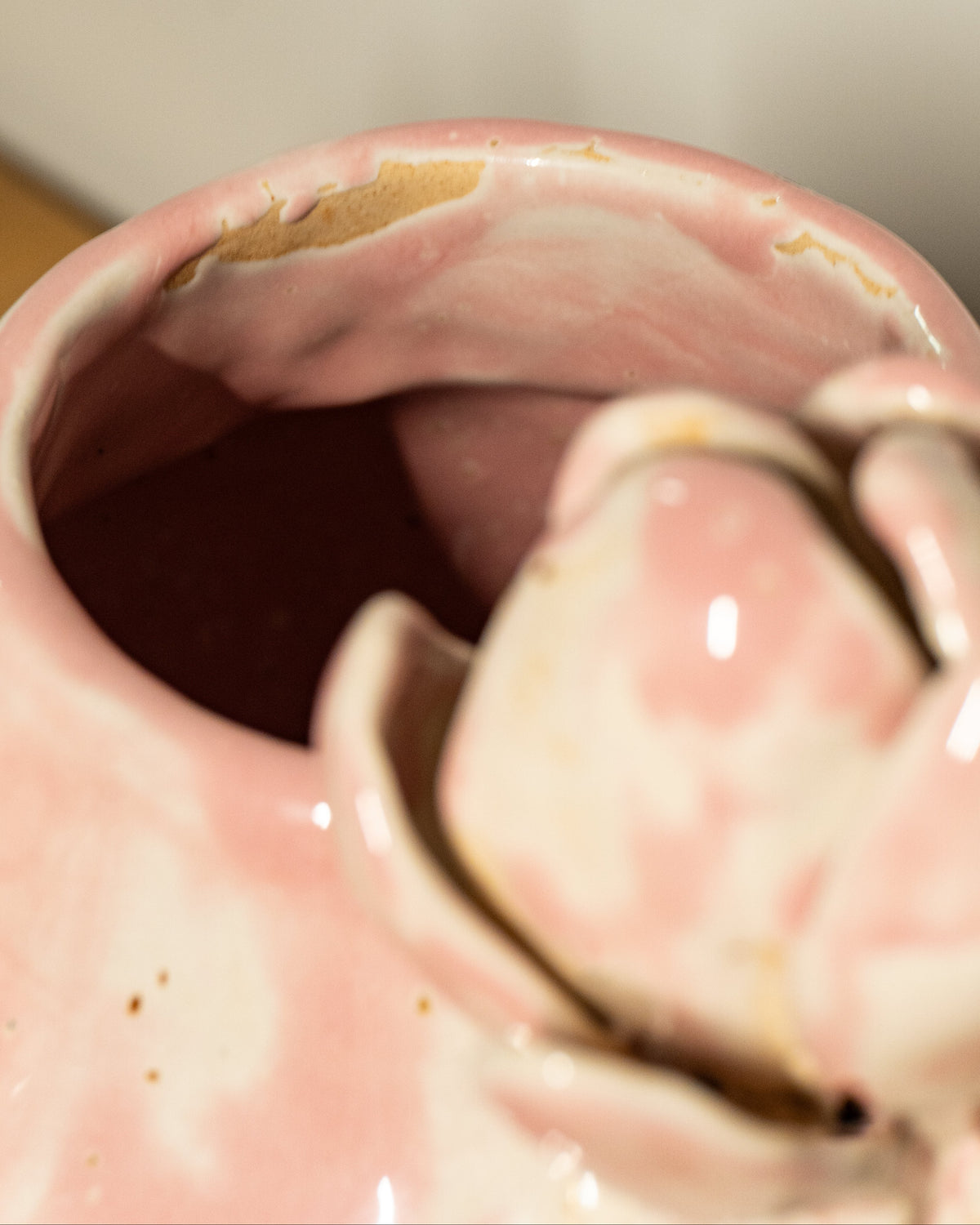 Close-up of a pink glazed ceramic vase, showing a glossy pink surface with a small area of exposed clay near the rim.